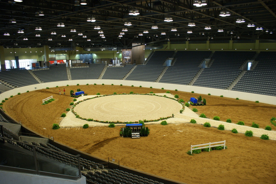 A photo of a equestrian performance arena with a round performance area surrounded by horse jumps.