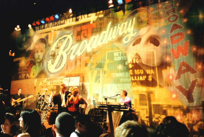 Singers on a stage with a Broadway backdrop.