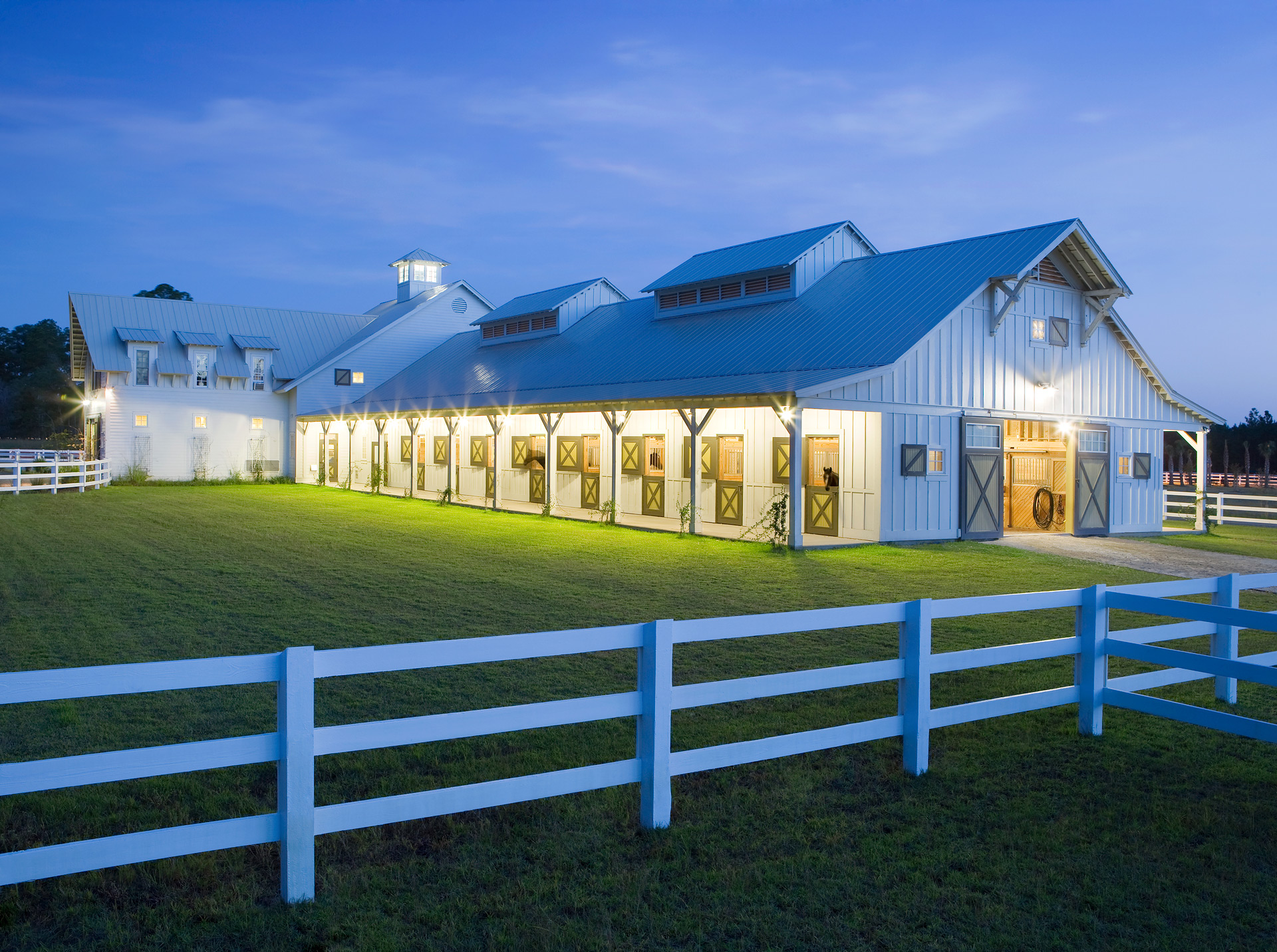 equestrian center at dusk with yellow lights and blue sky above green grass