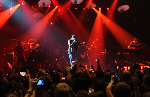 A singer on stage at a concert event with red spot lights lighting up the stage.