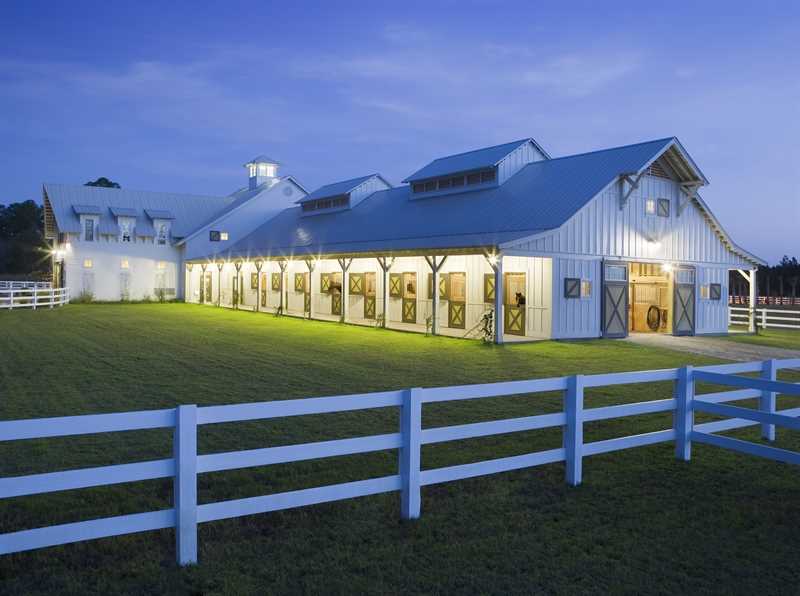 A horse barn with 8 stables lit up in front of a green pasture.