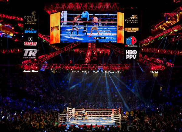 A heavy-weight boxing event being seen by a crowd in person and on a jumbo-tron.