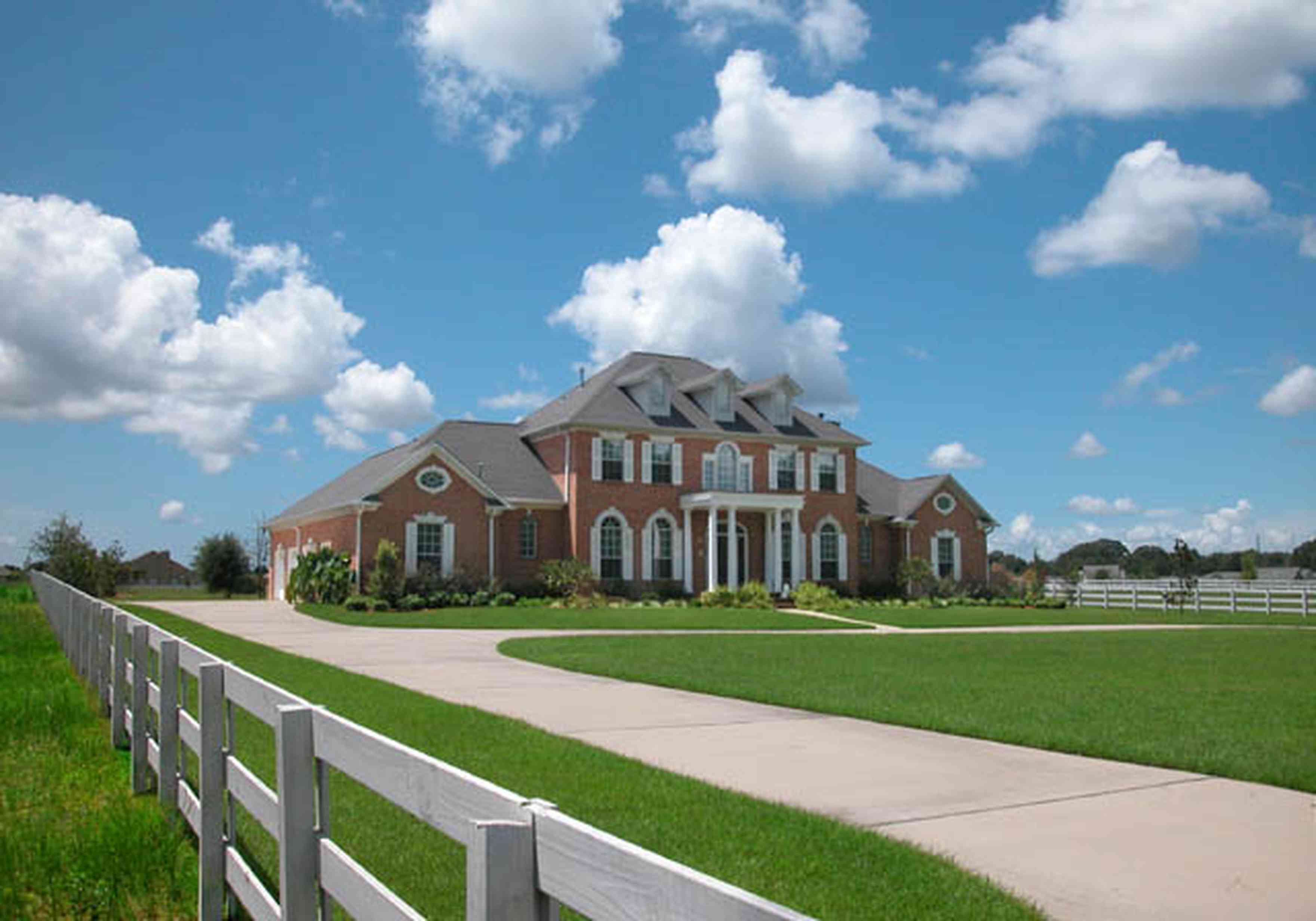A large red brick, 3 story Ranch House at the end of a long concrete driveway.