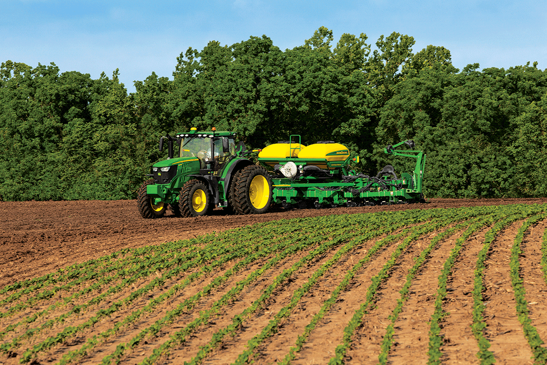 A green tractor driving through a newly planted field. 
